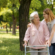 Pflegekraft hilft älterer Frau mit Gehhilfe im Freien