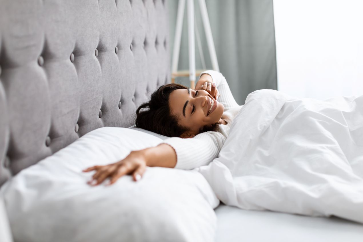 Junge Frau streckt sich laechelnd auf einem gepolsterten Boxspringbett – idealer Moment nach dem Boxspringbett kaufen