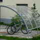Zwei Fahrräder unter einer modernen Fahrradüberdachung aus Metall und transparentem Kunststoff vor einem Wohngebäude