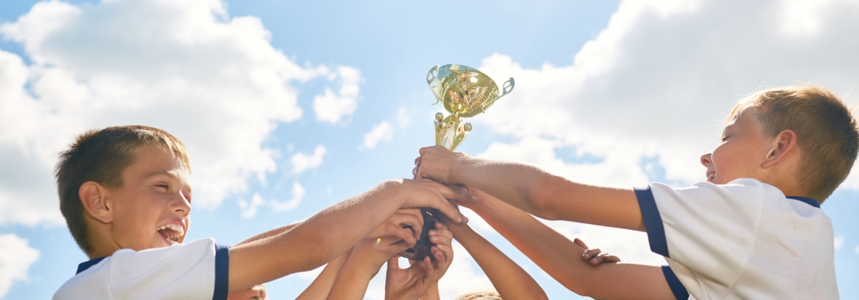 Kinder halten gemeinsam einen Pokal hoch als Zeichen für Teamgeist und Anerkennung im Sport